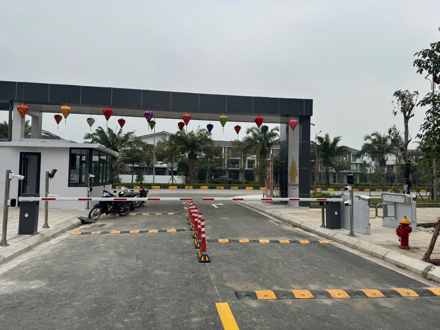 Cổng ra vào khu đô thị với hệ thống barrier tự động, chốt bảo vệ và xe máy đỗ bên trong